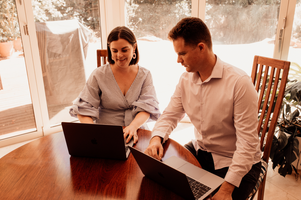 Carmen and DAvid sit at a dining table and send emails